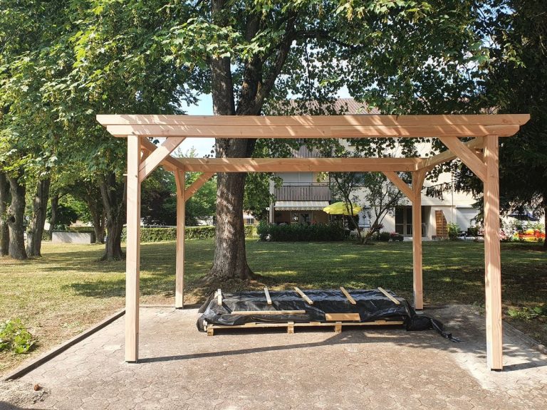 Carport-Konstruktion aus Holz im Rohbau unter Bäumen, noch ohne Dacheindeckung