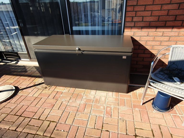 Anthrazitfarbene Mülltonnenbox auf Klinkerpflaster an der Hauswand