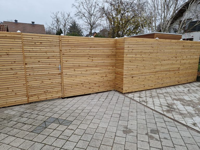 Holz-Sichtschutzzaun als Abgrenzung einer gepflasterten Hofeinfahrt