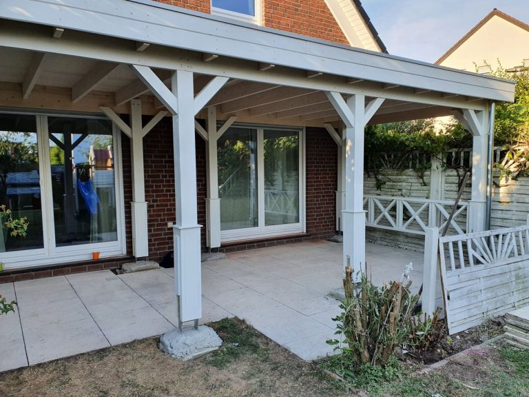 Weiß lackierte Terrassenüberdachung mit Säulen als Veranda vor einem Wohnhaus